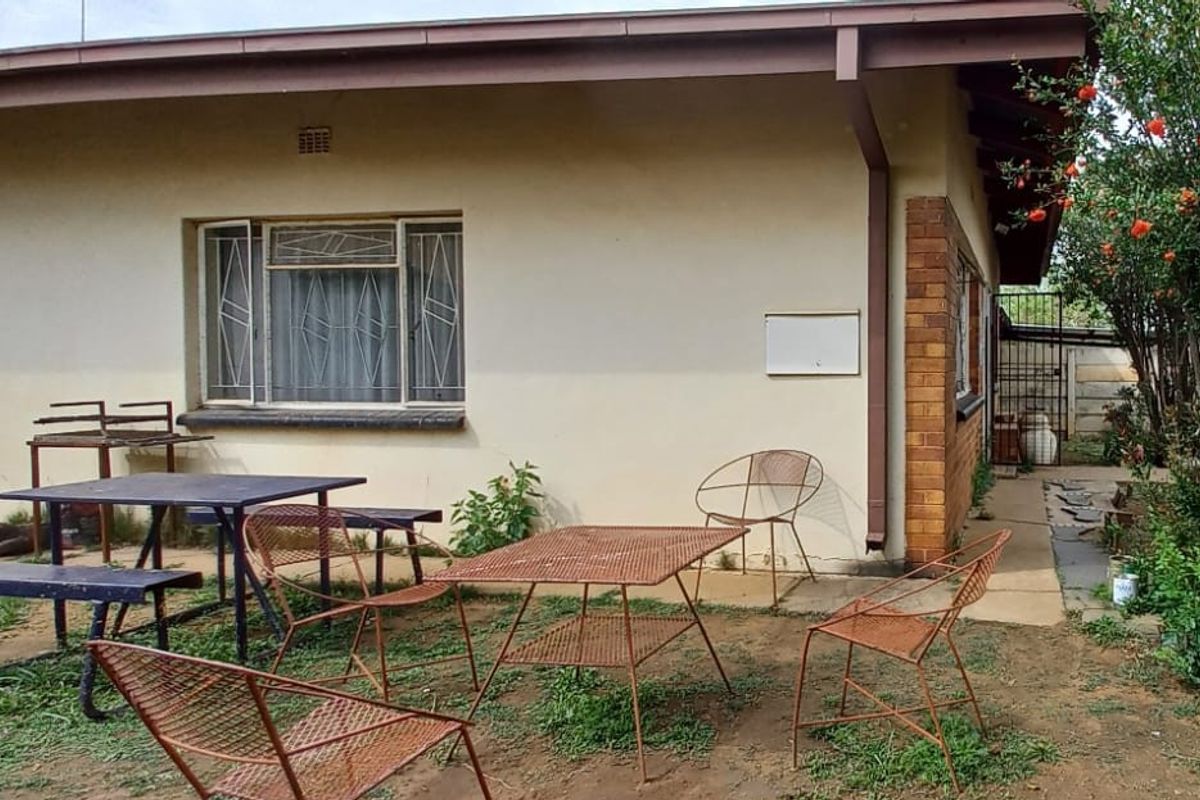 Rear exterior view of the house featuring a brick and plaster facade with security bars on the windows and a concrete pathway.