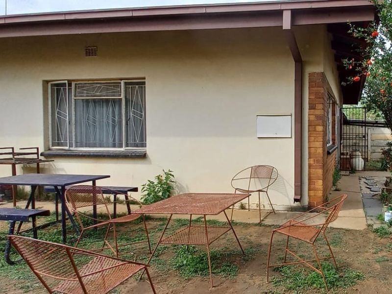 Rear exterior view of the house featuring a brick and plaster facade with security bars on the windows and a concrete pathway.