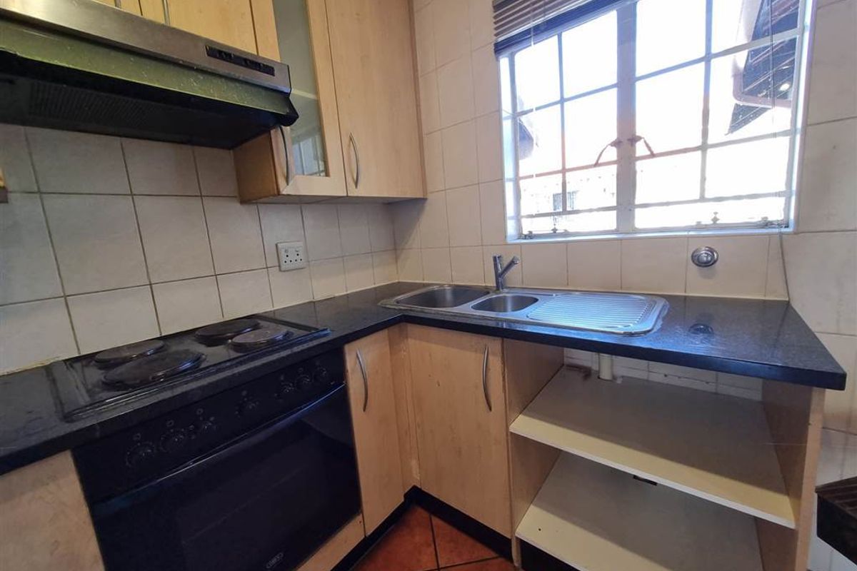 A functional kitchen featuring built-in cabinetry, a stainless steel sink, electric hob, and oven with tiled backsplash and flooring.