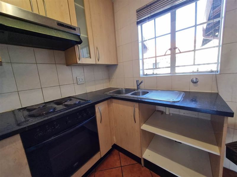 A functional kitchen featuring built-in cabinetry, a stainless steel sink, electric hob, and oven with tiled backsplash and flooring.