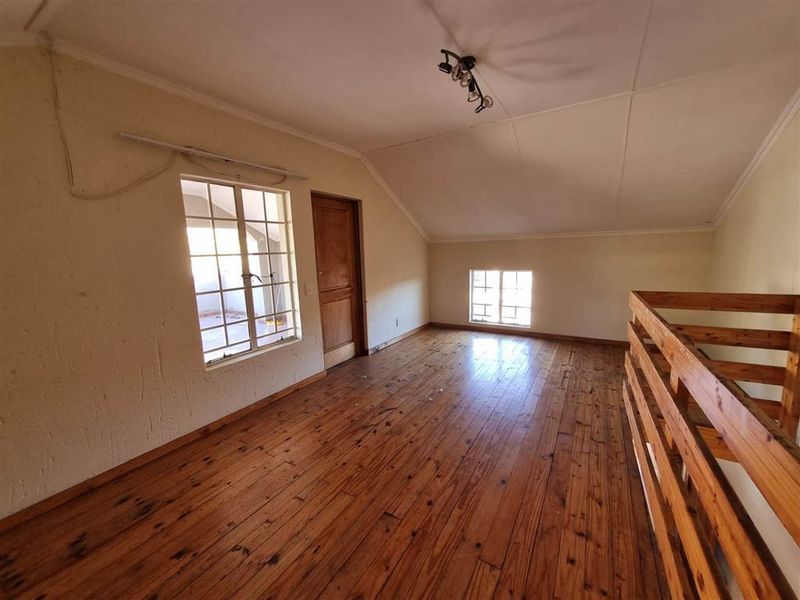 An empty loft-style bedroom featuring timber flooring, a wooden balustrade, and natural light from multiple windows.