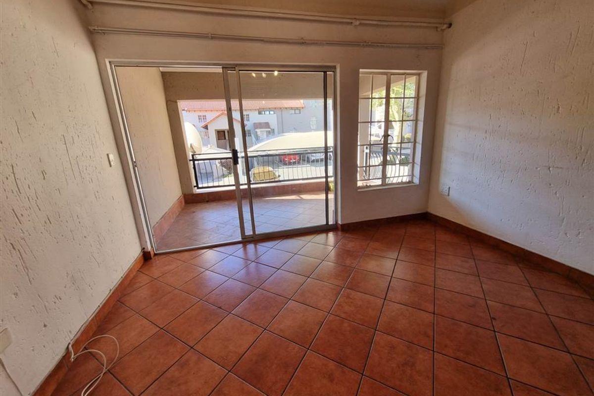 An empty living room featuring tiled flooring, a sliding glass door leading to a balcony, and a window with security bars.