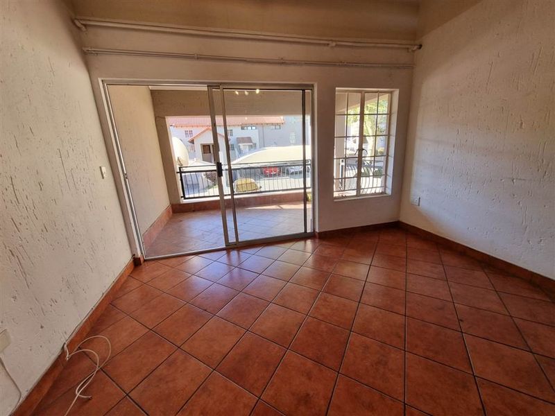 An empty living room featuring tiled flooring, a sliding glass door leading to a balcony, and a window with security bars.