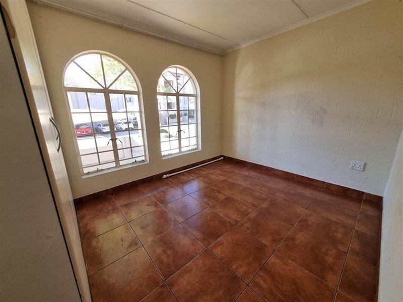 An empty bedroom featuring arched windows, tiled flooring, and a built-in cupboard, offering a blank canvas for potential renovation or staging.