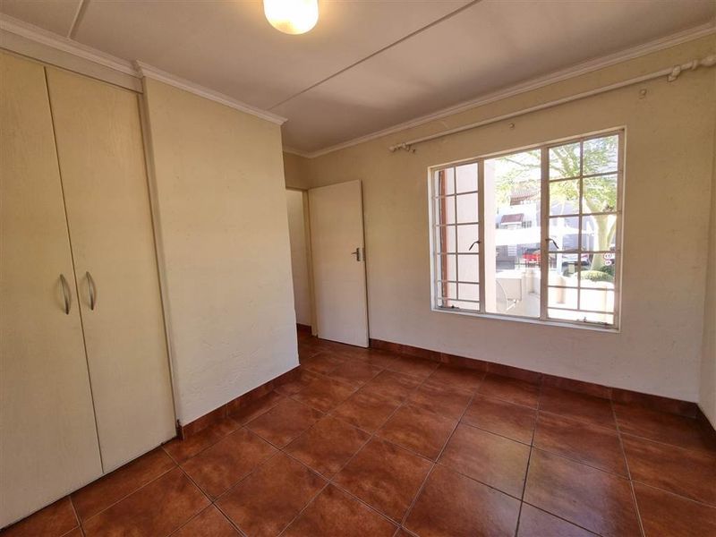 A vacant bedroom featuring tiled flooring, built-in cupboards, and a window with security bars, offering a blank canvas for personalization.