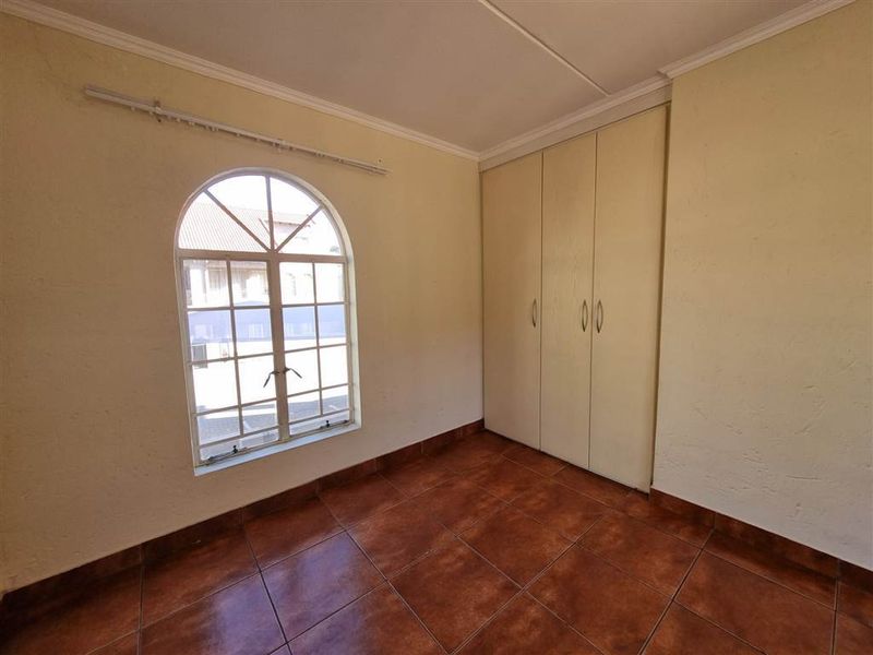 An empty bedroom featuring tiled flooring, built-in cupboards, and a distinctive arched window, offering a blank canvas for potential renovation.