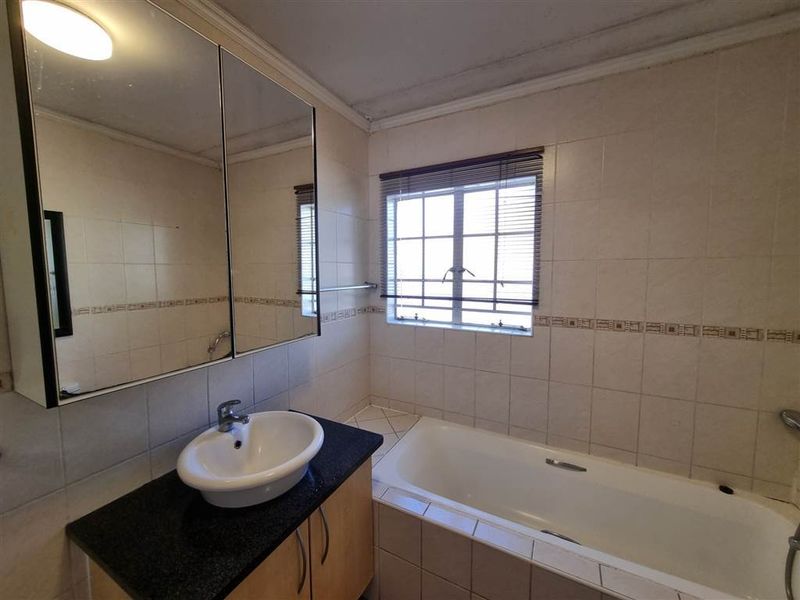 A functional bathroom featuring a vanity with a vessel sink, a medicine cabinet, and a built-in bathtub with tiled wall surrounds.