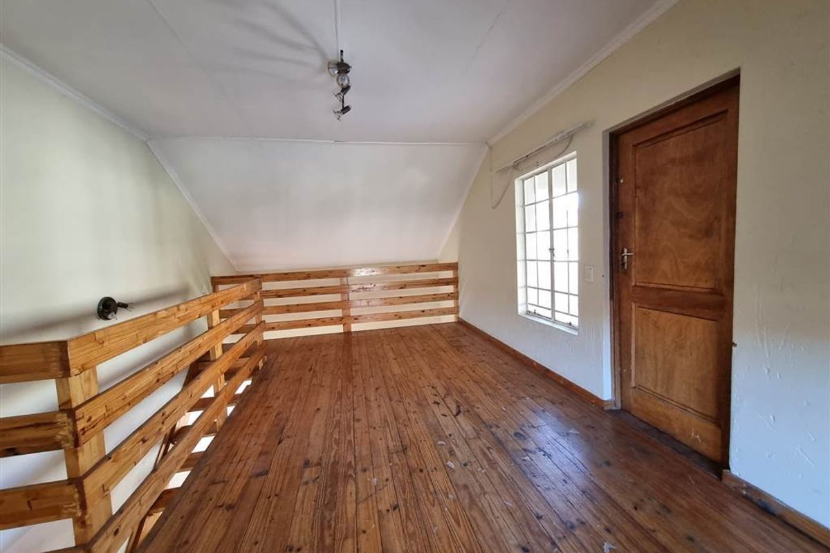 An empty loft-style bedroom featuring timber flooring, a wooden balustrade, and a single door, offering a rustic aesthetic ready for renovation or staging.