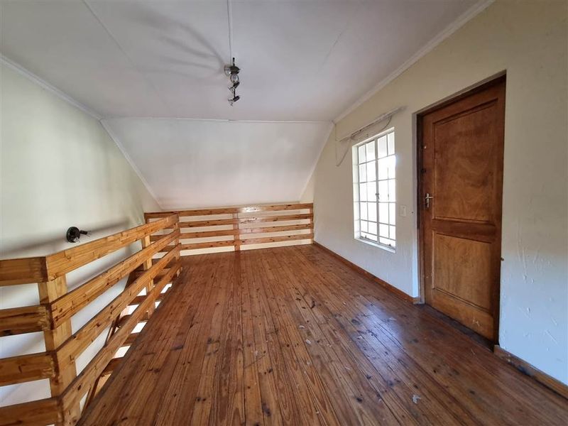 An empty loft-style bedroom featuring timber flooring, a wooden balustrade, and a single door, offering a rustic aesthetic ready for renovation or staging.
