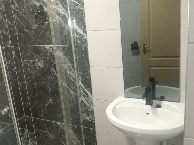 A modern bathroom featuring a pedestal basin with a black mixer tap, a glass shower enclosure, and contrasting marble-effect and white wall tiling.