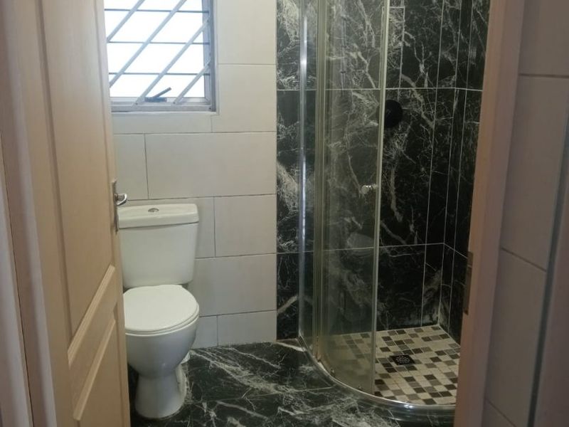 A compact bathroom featuring a corner shower enclosure, toilet, and contrasting black marble-effect floor and wall tiles.