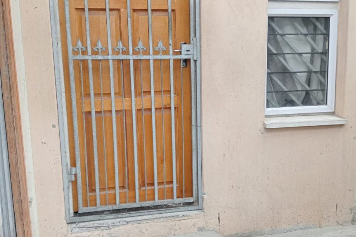 Exterior view of a rear entrance featuring a timber door with a security gate and an adjacent window with security bars.