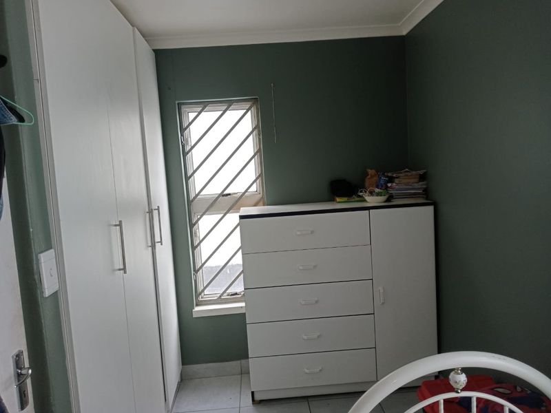 A bedroom featuring built-in cupboards, tiled flooring, and a window fitted with security bars, finished with dark green wall paint.