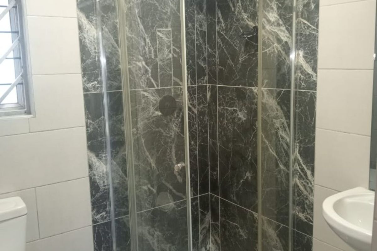 A modern bathroom featuring a curved glass shower enclosure, marble-look wall tiling, a pedestal basin, and a toilet.
