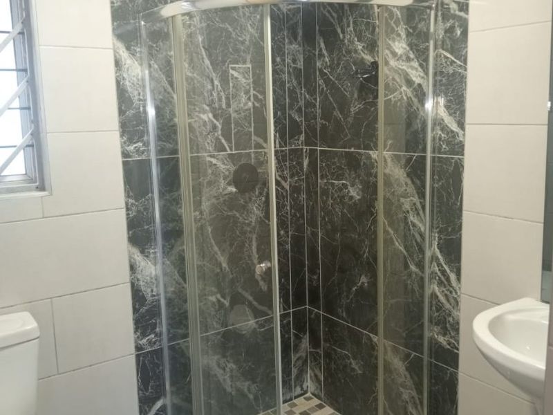 A modern bathroom featuring a curved glass shower enclosure, marble-look wall tiling, a pedestal basin, and a toilet.