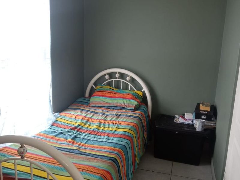 A compact bedroom featuring tiled flooring and neutral wall finishes, providing a functional space with natural light from the window.