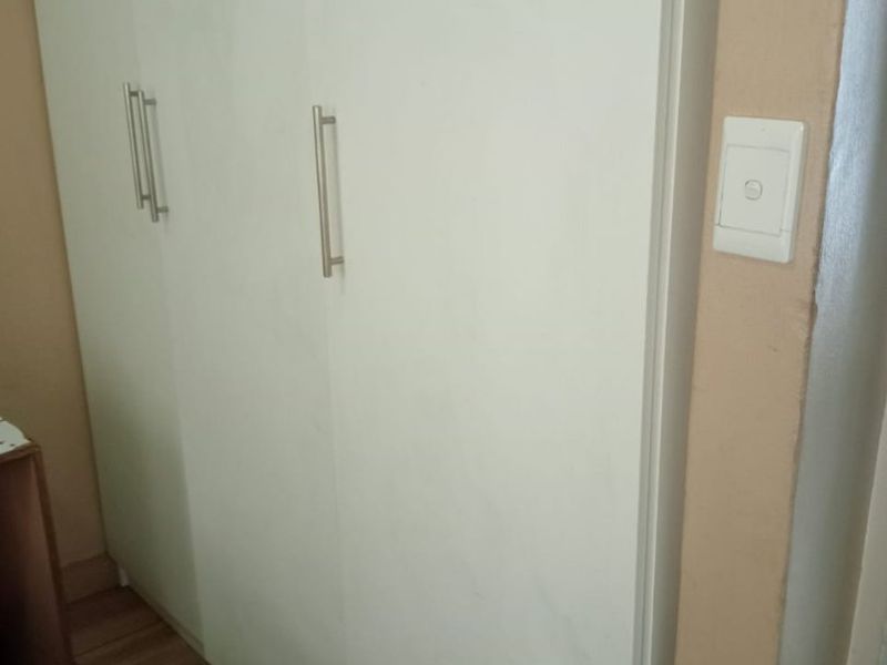 A bedroom interior featuring a clean, white built-in wardrobe with modern handles and tiled flooring.