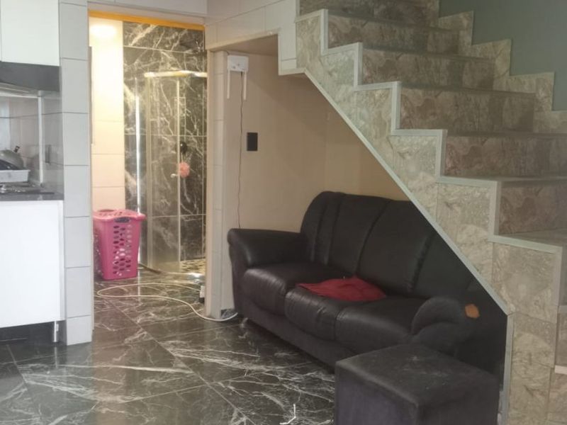 Open plan living area featuring marble-effect floor tiles, a timber ceiling, and a tiled staircase with integrated storage space, leading to a bathroom.