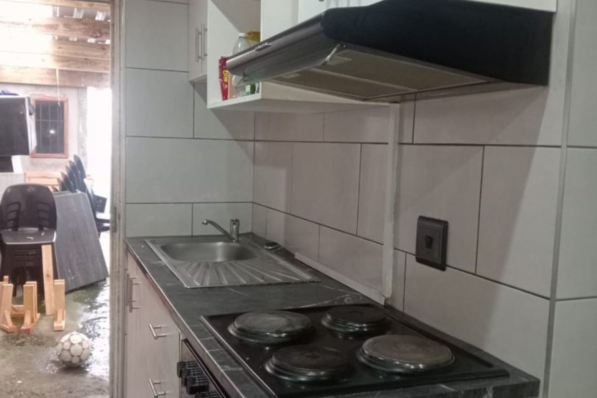 A functional kitchen featuring white cabinetry, a dark countertop, integrated electric hob, oven, extractor fan, and tiled finishes.