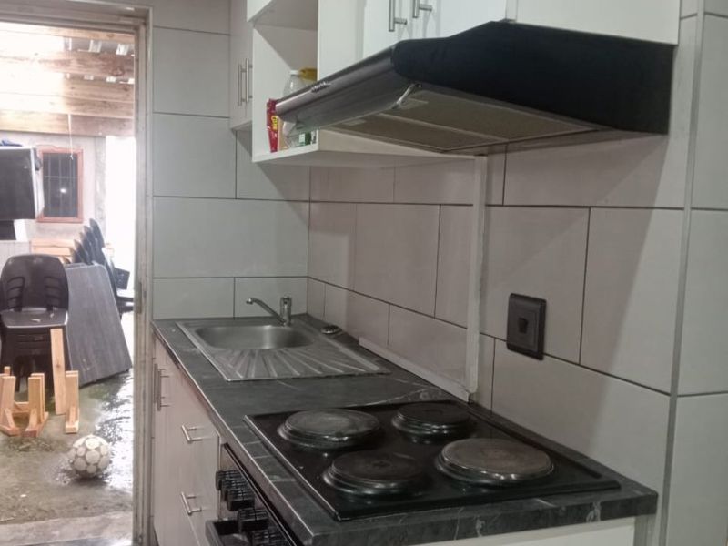 A functional kitchen featuring white cabinetry, a dark countertop, integrated electric hob, oven, extractor fan, and tiled finishes.