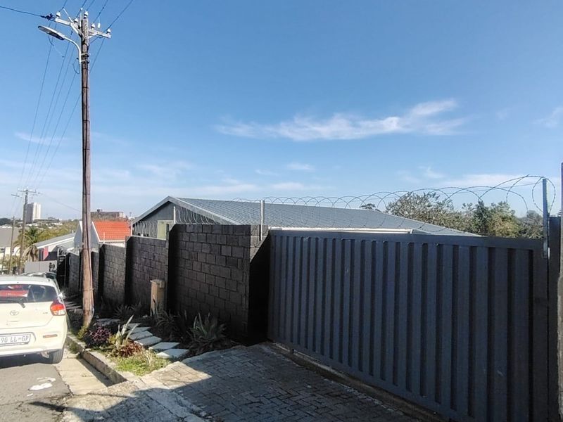 Front exterior view of the property featuring a secure sliding gate, concrete block boundary wall with razor wire, and a paved driveway.