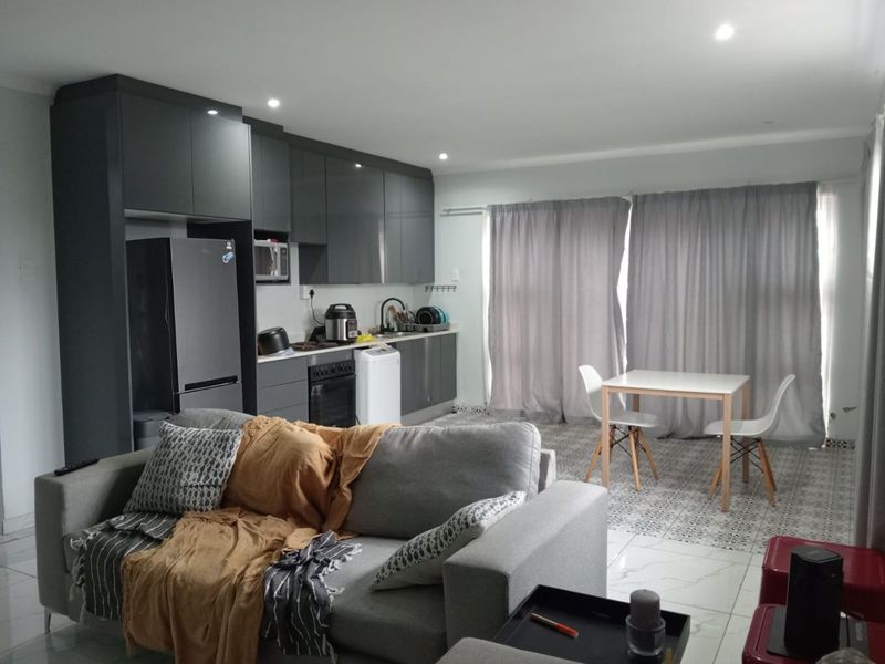 Modern open-plan living area featuring a sleek kitchen with dark cabinetry, integrated appliances, and tiled flooring throughout the combined kitchen and dining space.