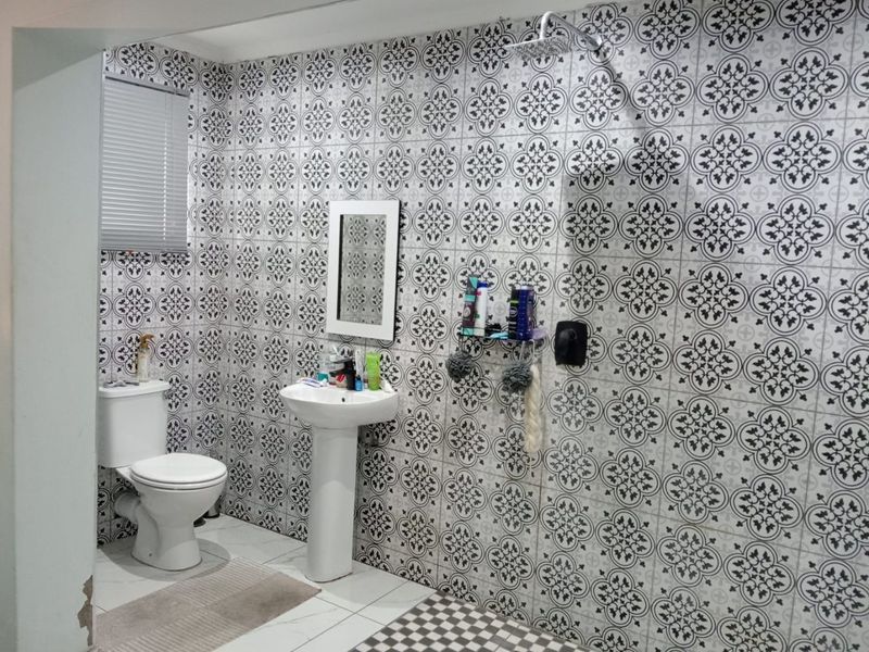 A bathroom featuring patterned wall tiles, a pedestal basin, a toilet, and a shower head with a modern aesthetic.