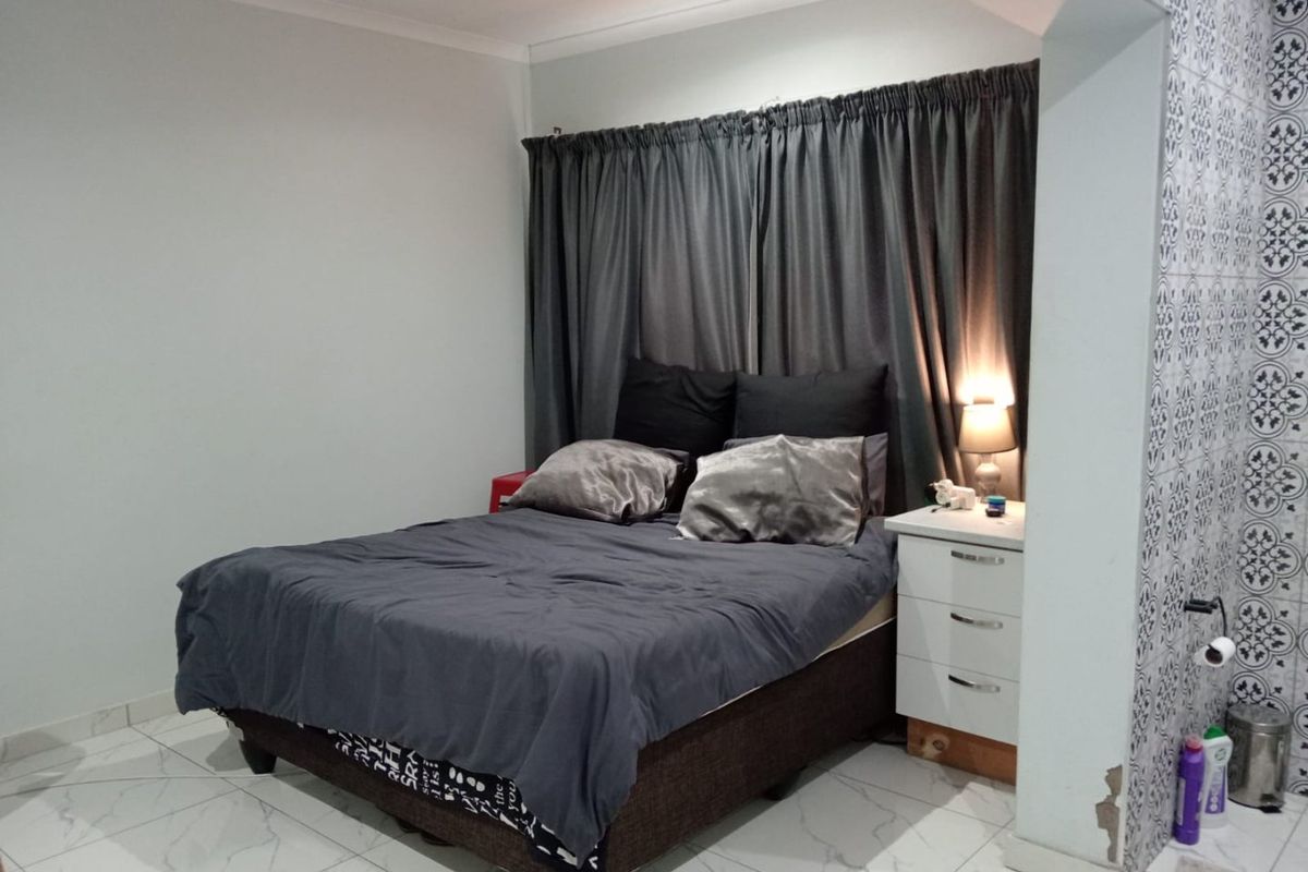 A bedroom featuring tiled flooring and a decorative tiled accent wall, with visible plaster damage at the base of the structural pillar.