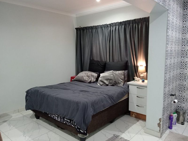 A bedroom featuring tiled flooring and a decorative tiled accent wall, with visible plaster damage at the base of the structural pillar.