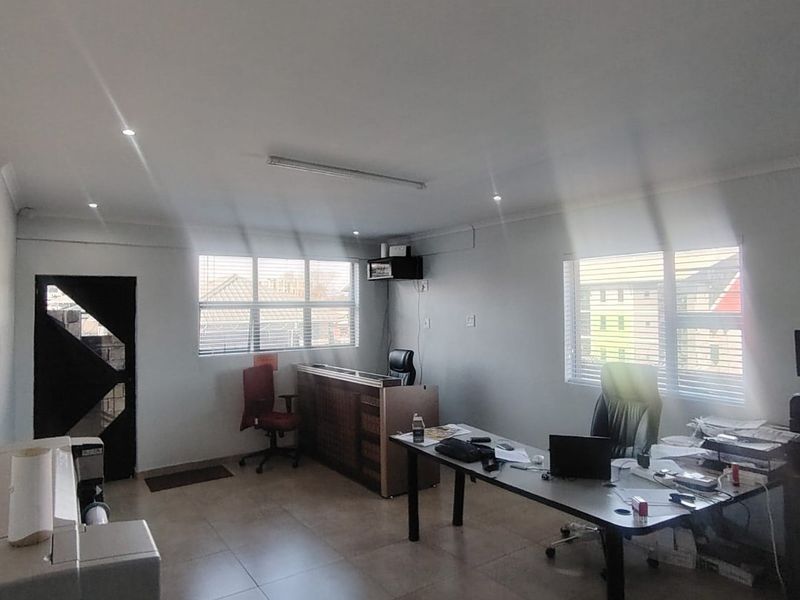A functional office space featuring tiled flooring, recessed downlighting, and large windows with venetian blinds, providing a bright and practical work environment.