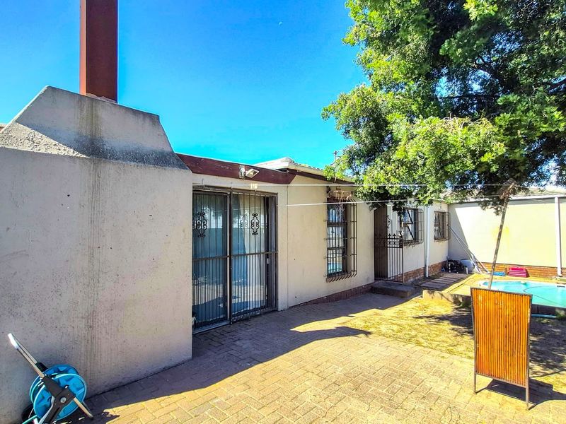 Rear exterior view of the property featuring a paved patio area, a swimming pool, and a prominent chimney stack.