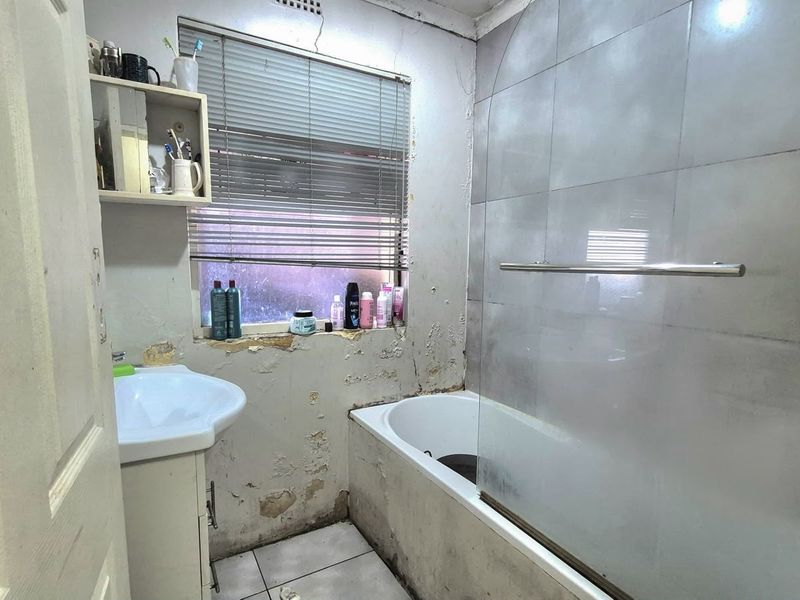 A bathroom featuring a bathtub with a glass screen and a pedestal basin, currently requiring significant wall repairs and cosmetic updates.