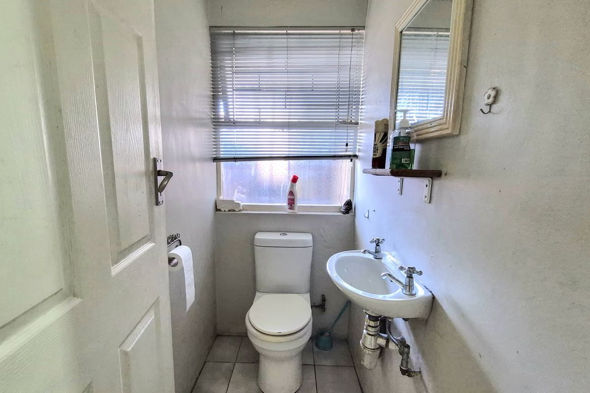 A compact guest bathroom featuring a wall-mounted basin, toilet, and tiled flooring, requiring cosmetic updates to improve its overall condition.