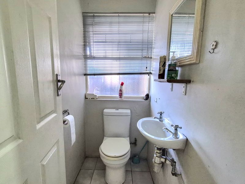 A compact guest bathroom featuring a wall-mounted basin, toilet, and tiled flooring, requiring cosmetic updates to improve its overall condition.