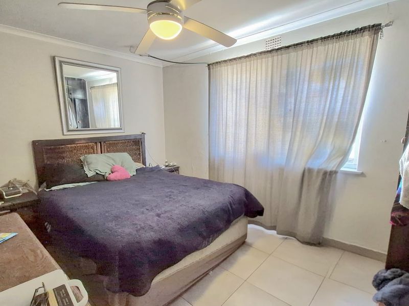 A functional bedroom featuring tiled flooring, a ceiling fan, and a window with curtains, providing a neutral base for personalization.