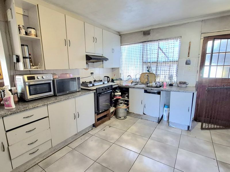 A functional kitchen featuring built-in cabinetry, a gas stove with oven, and tiled flooring, offering potential for modernization and cosmetic updates.