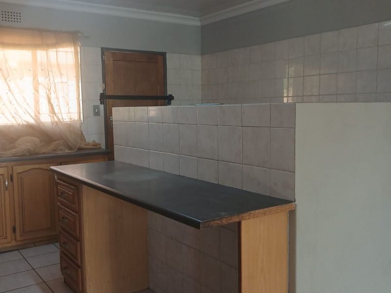 A dated kitchen area featuring tiled flooring, built-in cabinetry, and a tiled splashback, offering a functional layout ready for modernization.