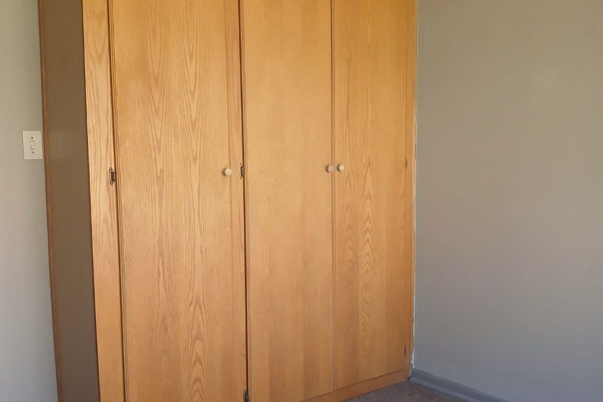 A bedroom featuring a built-in wooden wardrobe and carpeted flooring, offering a neutral space ready for personalization.