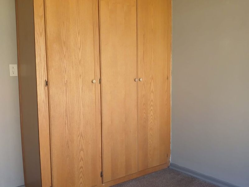 A bedroom featuring a built-in wooden wardrobe and carpeted flooring, offering a neutral space ready for personalization.
