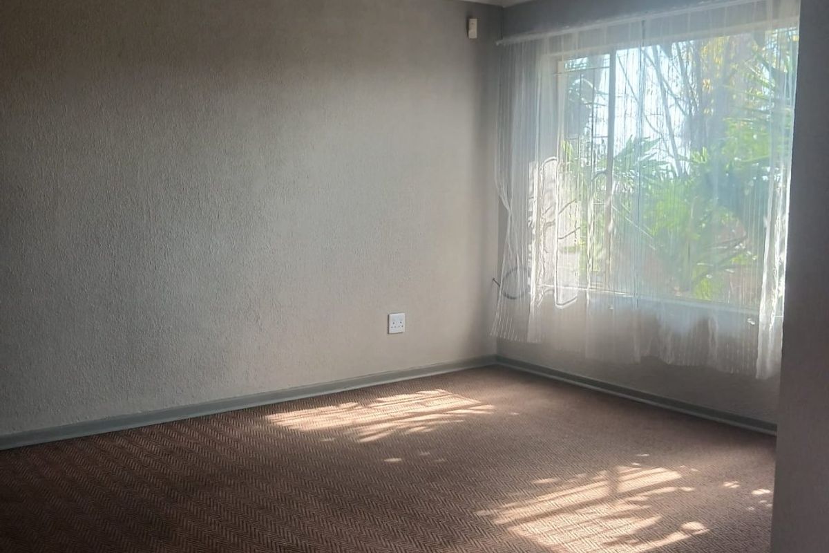 A bright, empty living room featuring neutral walls, carpeted flooring, and a ceiling fan, offering a versatile space ready for personalization.