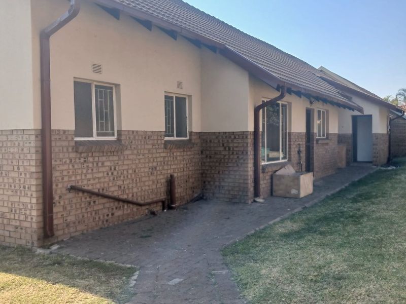 Rear view of the house featuring a brick and plaster facade, tiled roof, and a paved walkway leading along the side of the property.