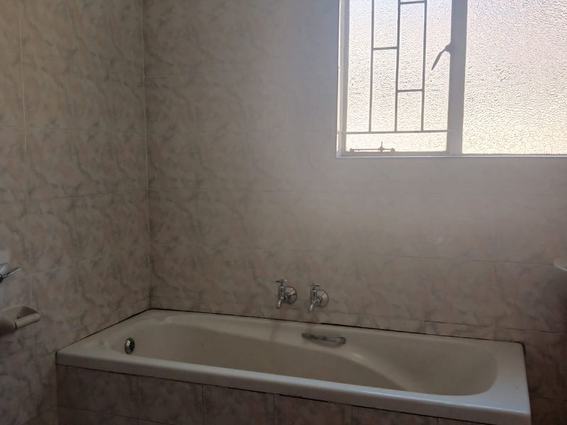 A dated bathroom featuring a built-in bathtub with tiled surround and a window with security bars.