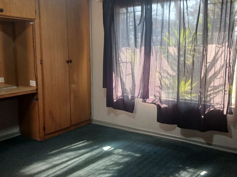 A bedroom featuring built-in wooden cabinetry with an integrated desk, carpeted flooring, and a window with security bars.