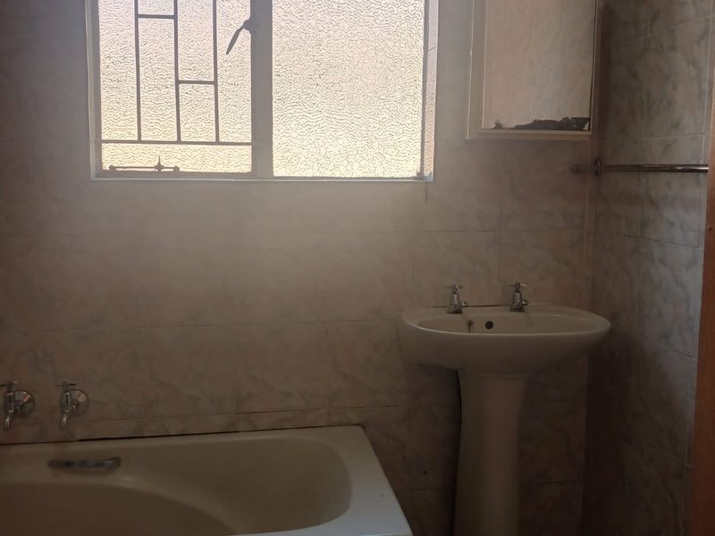A dated bathroom featuring a built-in bathtub, pedestal basin, and tiled walls, requiring modernization to improve its aesthetic and functionality.