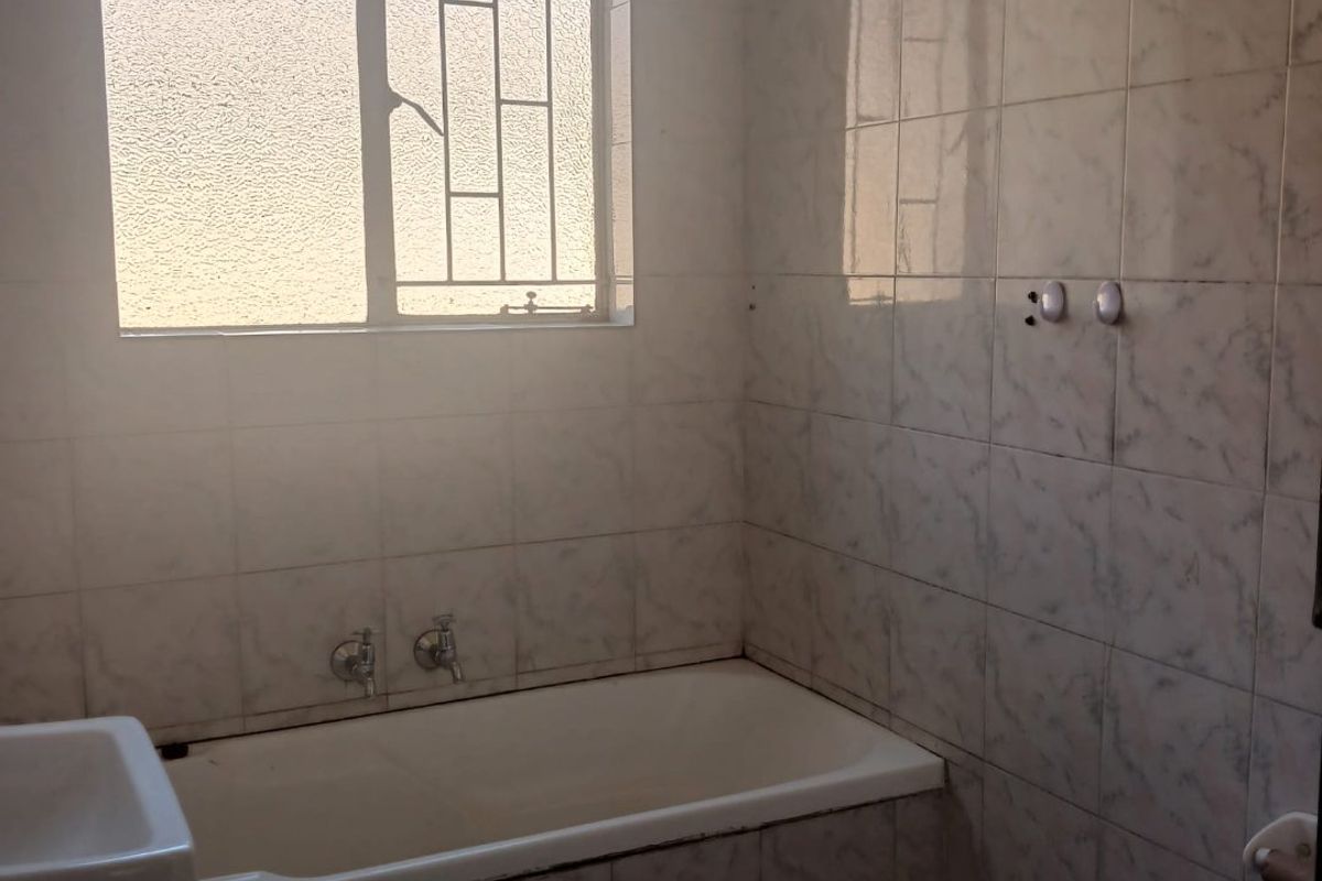 A dated bathroom featuring a built-in bathtub, wall-mounted basin, and tiled walls, requiring modernization to improve its aesthetic and functionality.
