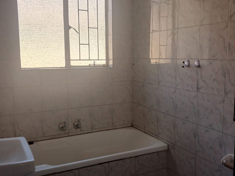 A dated bathroom featuring a built-in bathtub, wall-mounted basin, and tiled walls, requiring modernization to improve its aesthetic and functionality.