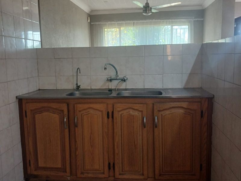 A functional scullery area featuring wooden cabinetry, a double sink with tiled splashback, and a ceiling fan, offering a practical utility space.