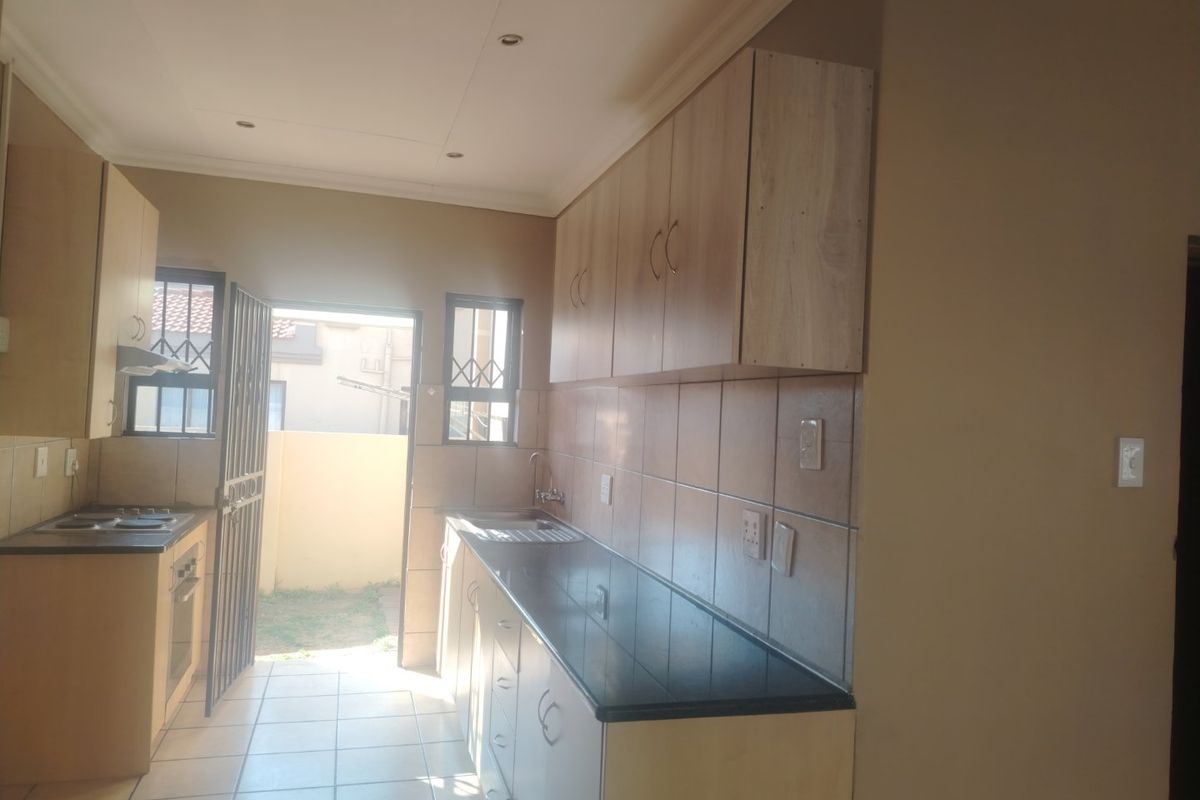 A functional kitchen featuring light wood-finish cabinetry, dark countertops, tiled backsplash, and direct access to an outdoor area through a security gate.