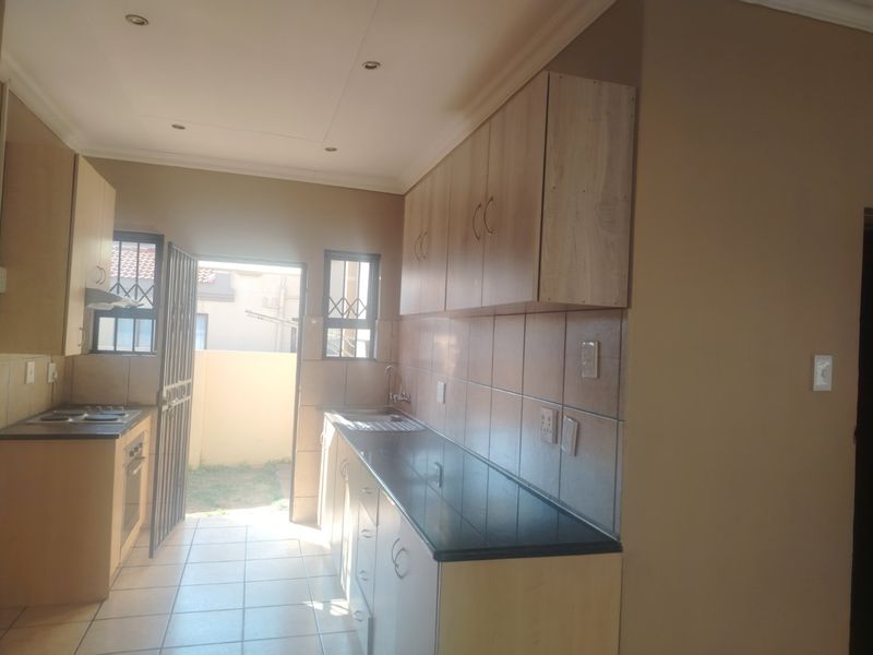 A functional kitchen featuring light wood-finish cabinetry, dark countertops, tiled backsplash, and direct access to an outdoor area through a security gate.