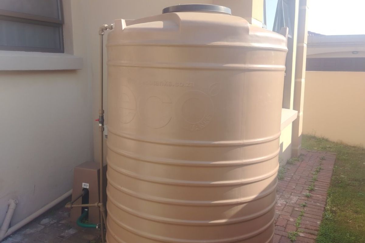 An exterior view of the property featuring a large, installed water storage tank positioned alongside the building structure on a paved area.